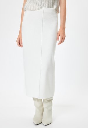 Witte gebreide kokerrok met een verticale naad, in combinatie met kniehoge witte stoffen laarzen met een spitse neus. Geweven oppervlakte detail.