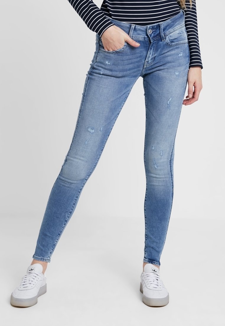 Blå denim skinny jeans med en bleknad tvätt, slitna detaljer, femfickorsdesign och midjehöjd, parat med vita sneakers.