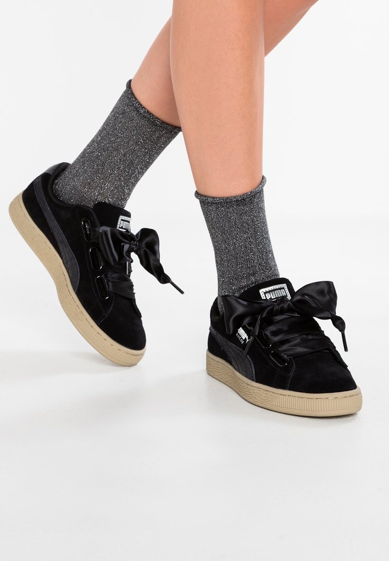 Czarne zamszowe sneakersy z satynowymi sznurówkami, z beżową gumową podeszwą i metalicznymi akcentami. Noszone z błyszczącymi szarymi skarpetkami.