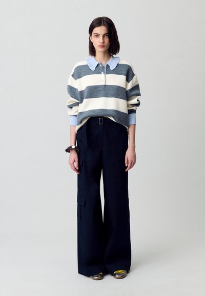Maglione a righe in crema e grigio con colletto blu, abbinato a pantaloni a vita alta blu navy a gamba larga con tasche cargo e cintura.