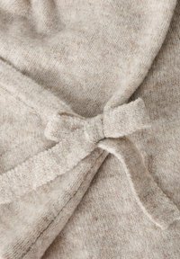 Pletenina v kremni barvi z mehko teksturo, ki ima detajl z navezanim lokom. Tkanina ima subtilen črtast vzorec skozi celotno površino.