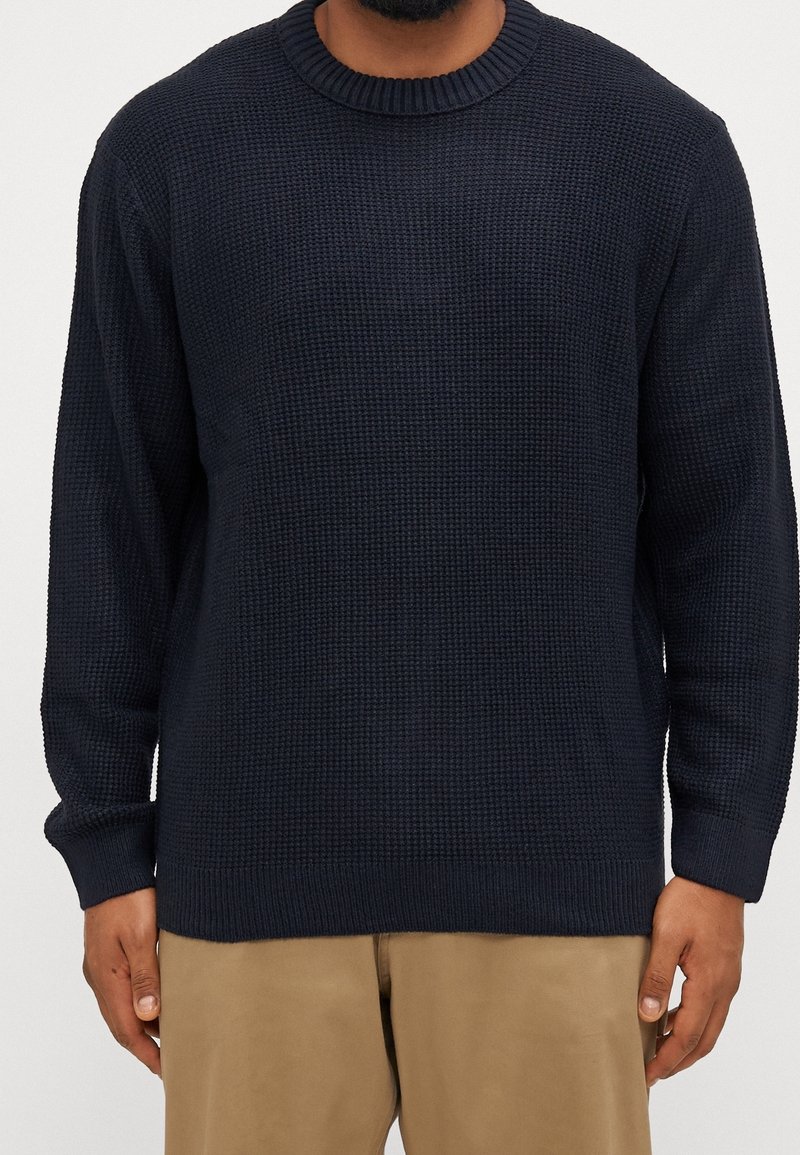 Mörkblå stickad tröja med rund hals, prydd med ett texturelement och långa ärmar, tillverkad av ett mjukt, tjockt material.