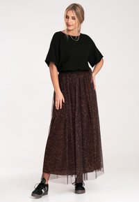 Czarny sweterek dziany w połączeniu z długą, przezroczystą spódnicą z brązowego tiulu z delikatnym wzorem w panterkę, uzupełnioną czarnymi trampkami sportowymi.