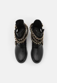 Botas de tobillo de cuero negro con una gruesa cadena dorada alrededor del caño, con una textura suave y puntera redondeada.