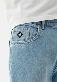 Ljusblå denimjeans med orange sömmar och en svart diamantformad logotypapplikation på bakfickan; texturerad tyg, slim fit.