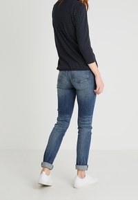 Námořnické tričko s puntíky a dlouhým rukávem zkombinované se světle modrými slim-fit džíny, se zahnutými manžetami a bílými teniskami na neutrálním pozadí.