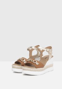 Brown and gold wedge sandals featuring a braided jute midsole, metallic accents, and an adjustable ankle strap with a buckle.