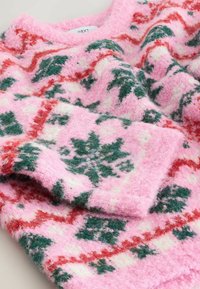 Ružový pletený sveter s jemnou, nadýchanou textúrou a zelenými a červenými kvetinovými vzormi. Má okrúhly výstrih a dlhé rukávy.