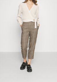 Krémový pletený svetřík s páskem; hnědé kárované vysoké krátké kalhoty; černé mokasíny s řetízkovým zdobením.