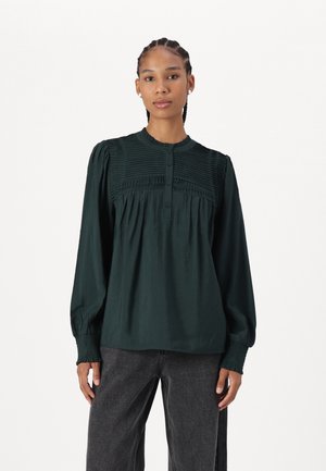 Dark green blouse with long sleeves, button front, and pleated design at the chest. Made of a smooth fabric, featuring gathered cuffs.