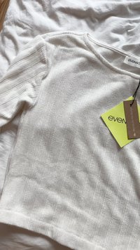 Top bianco a coste con maniche lunghe. Caratterizzato da un collo rotondo e un'etichetta che mostra "even&odd" e dettagli sul materiale. Texture morbida.