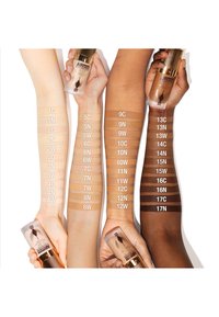 Airbrush foundation bottles held next to various arms displaying skin tone swatches. Swatches labeled with shade numbers, ranging from light to dark.