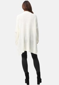 Leichte, übergroße weiße Strickjacke mit geripptem Kragen und offenem Rücken, kombiniert mit schwarzen Leggings und Stiefeletten.