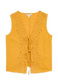 Gul ärmlös blus med broderad blommönster och utskurna detaljer, som har en knytning fram och vågig nederkant.