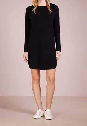 Sort strikket kjole med lange ærmer, rund halsudskæring og sidelæg, parret med hvide sneakers på en neutral baggrund.
