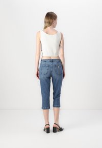 Top court blanc, jeans bleu taille moyenne à coupe slim avec deux poches arrière, et sandales à talons noires avec un bout carré.