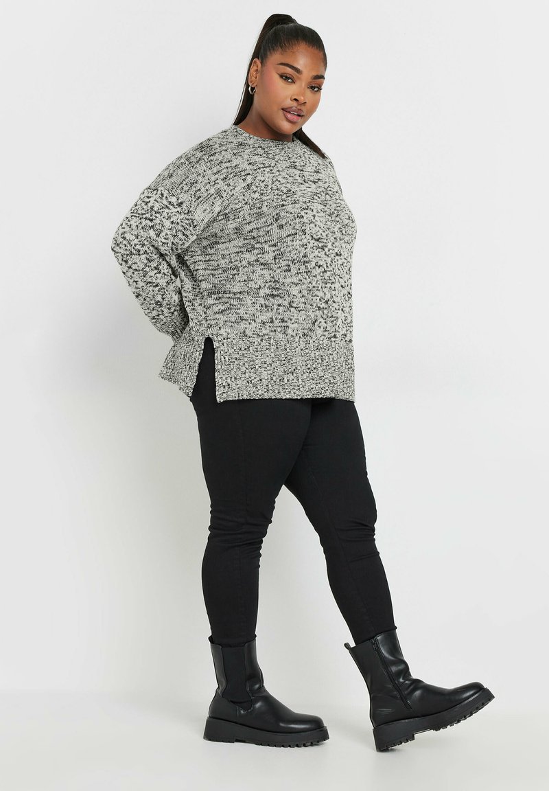 Grå och svart stickad tröja med avslappnad passform, sidokliå, och ribbad struktur, parat med figurnära svarta byxor och kraftiga svarta stövlar.