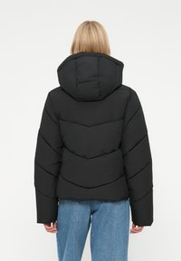 Sort polstret jakke med hætte, der har et chevron-mønster og en cropped pasform; båret med lyseblå løstsiddende jeans.