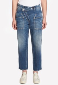 Jeans de mezclilla azul con corte relajado, que cuentan con dos grandes bolsillos frontales, una bragueta de botones y un ligero desgaste en los muslos.