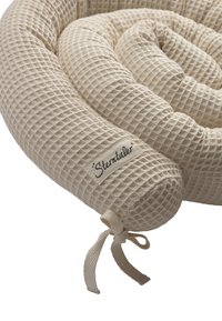Woven fabric baby bumper in light beige, featuring a textured grid pattern and a tied end. Stentaler brand label attached.