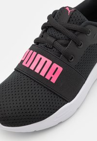 Baskets de sport noires avec tige en mesh, bande de logo rose et semelle blanche ; dotées de lacets et d'une texture perforée pour la respirabilité.