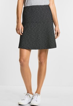 Une jupe noire avec un motif texturé, de forme évasée et de longueur mi-cuisse, portée avec des baskets blanches et un t-shirt gris.