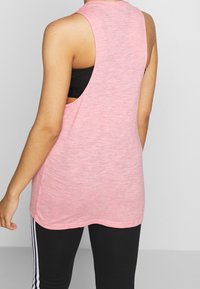 Růžová bezramínková tílko z lehké látky, s volným střihem a odkrytými boky, přes černé sportovní legíny.