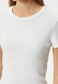 Hvid ribbet T-shirt med korte ærmer og rund halsudskæring. Stoffet ser blødt ud med en subtil struktur. Sømdetaljerne er minimale.