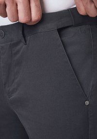 Szare spodnie wykonane z teksturowanej tkaniny, z tradycyjnym paskiem w talii, zapinanym na guzik oraz skośnymi kieszeniami bocznymi.