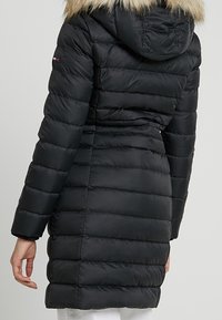 Chaqueta acolchada negra con capucha con ribete de piel, que presenta secciones acolchadas horizontales, cintura ajustada y mangas largas.