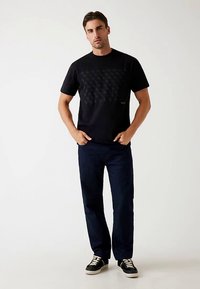 Black cotton t-shirt with a textured pattern on the front, paired with dark denim pants and black sneakers with white laces.