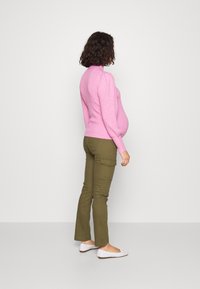 Pink ribbed sweater with a high neck, paired with olive green cargo pants, and white slip-on shoes. Model is shown from the side.