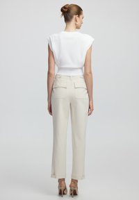 Top blanco sin mangas con un diseño ajustado, emparejado con pantalones crema a medida que presentan dos bolsillos traseros y dobladillos con vuelta. Sandalias de tacón plateadas.