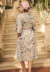 Šaty z lehké látky s květinovým vzorem, rukávy do loktů, vázané v pase, s živými barvami; nošeny s růžovo-bílým pruhovaným šátkem na hlavě.