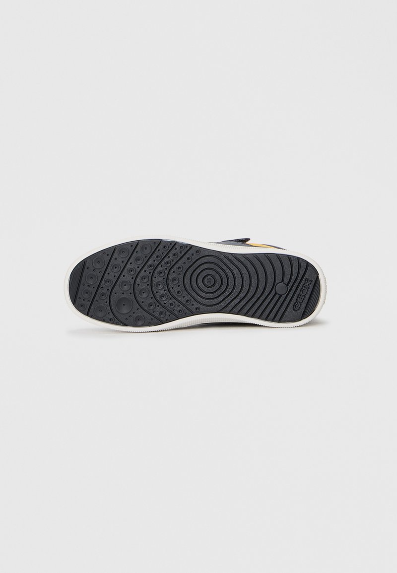 Suola di scarpa in gomma nera con superficie testurizzata, caratterizzata da motivi circolari e a onda, bordata da un margine bianco. Presente il logo Geox.