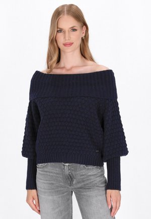 Marineblauwe gebreide trui met een off-shoulder ontwerp, geribbelde halslijn en een structuur met stippen. Wijde mouwen en aansluitende manchetten.