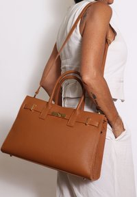 Borsa a mano in pelle tan con superficie liscia, doppi manici, tracolla rimovibile, hardware color oro e forma rettangolare strutturata.