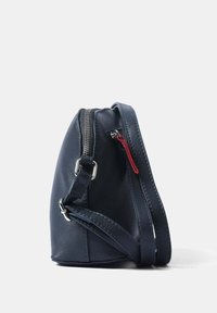 Borsa a tracolla in pelle blu navy con superficie texturizzata, chiusura superiore con zip, un tirazip rosso e tracolla regolabile. Forma rotonda con dettagli laterali.