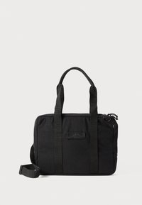 Svart tygväska med dubbla handtag upptill, justerbar axelrem och dragkedjestängning. Har en framtill placerad etikett och en minimalistisk design.