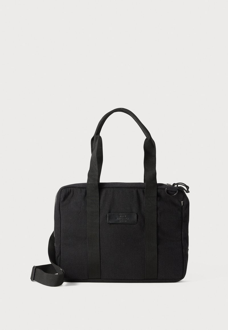Svart tygväska med dubbla handtag upptill, justerbar axelrem och dragkedjestängning. Har en framtill placerad etikett och en minimalistisk design.