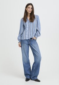 Blouse à rayures bleues avec manches volumineuses, associée à un jean en denim évasé et taille haute. La tenue présente une coupe décontractée et un tissu léger.