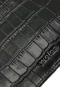 Czarna teksturowana powierzchnia ze wzorem krokodyla oraz srebrne logo "Wojas" wytłoczone w prawym dolnym rogu.