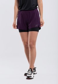 Lila sportshorts med svart innervadd, med sidsprund och en logotyp på benet. I kombination med svarta och vita sportskor.