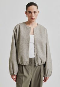 Grå fleecejakke med rund hals, glidelåslukking og puffede, lange ermer. Kombinert med høytlivede, lys grønne bukser.