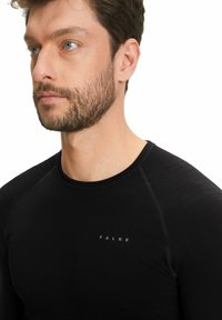 Zwart sportshirt met lange mouwen, voorzien van gestructureerde schouderpanelen en een logo. Gemaakt van gladde, rekbare stof voor comfort en prestaties.