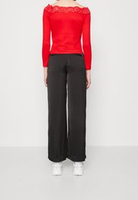 Röd långärmad topp med avtagbar spetsdetalj på axlarna, matchad med svarta vida byxor. Mjuk textur, avslappnad passform, vita sneakers.