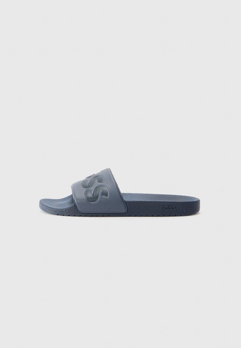 Blå sko med gummioverdel som har hevet logo, teksturert innersåle og flat såle for komfort. Designet er minimalistisk.