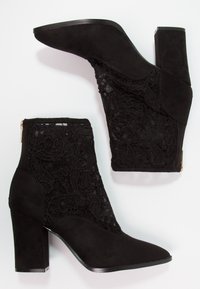 Botas de tobillo negras de ante con paneles laterales de encaje, con un tacón grueso y un cierre de cremallera en la parte trasera para facilitar su uso.
