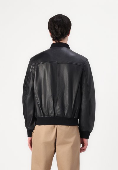 Veste bomber en cuir noir avec poignets et col côtelés, présentant une texture lisse et des coutures le long du dos pour un look ajusté.