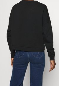 Felpa nera corta con maniche lunghe e polsini a coste, dalla texture liscia e vestibilità comoda, abbinata a jeans blu scuro.